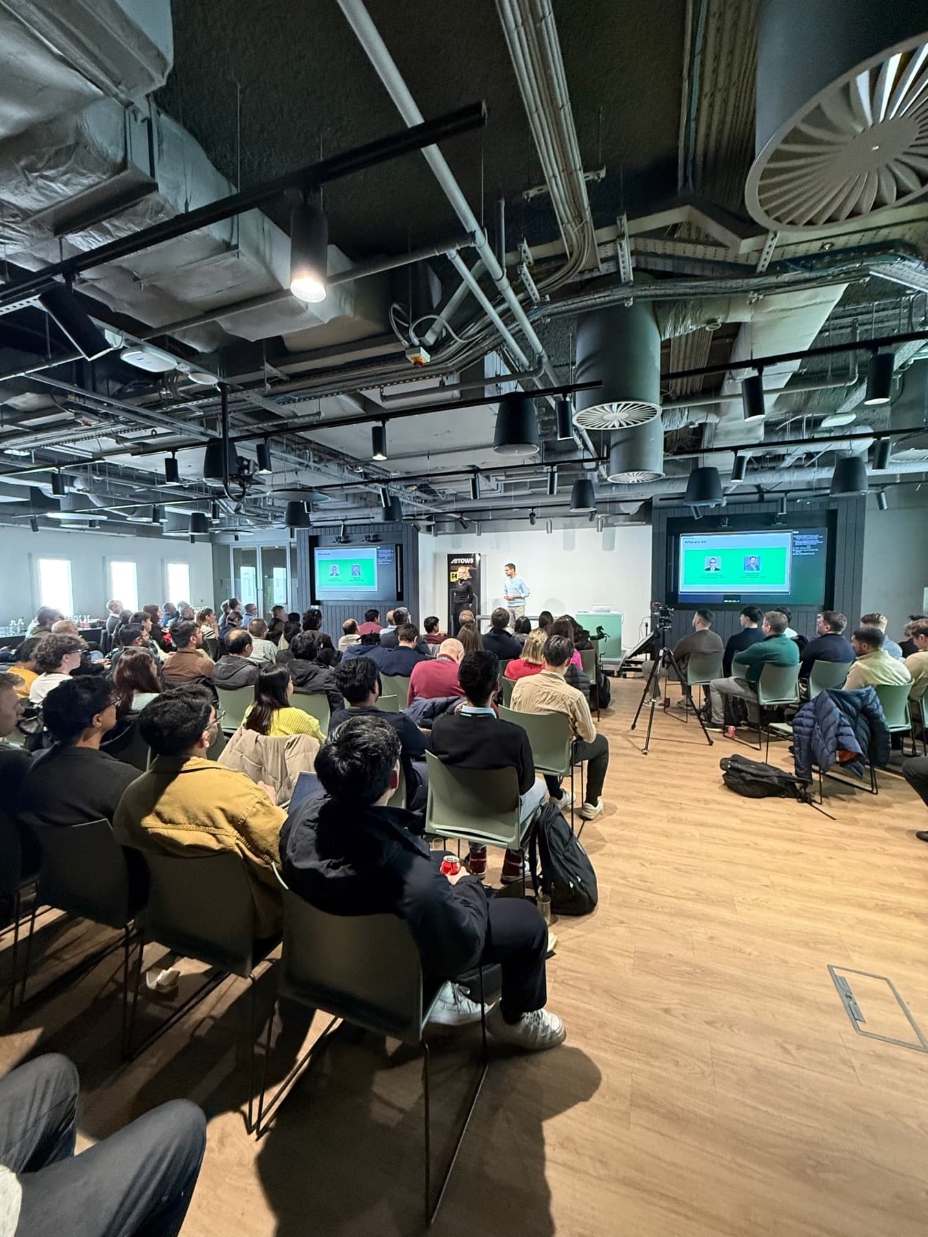 Attendees filling the room in front of two presentation screens