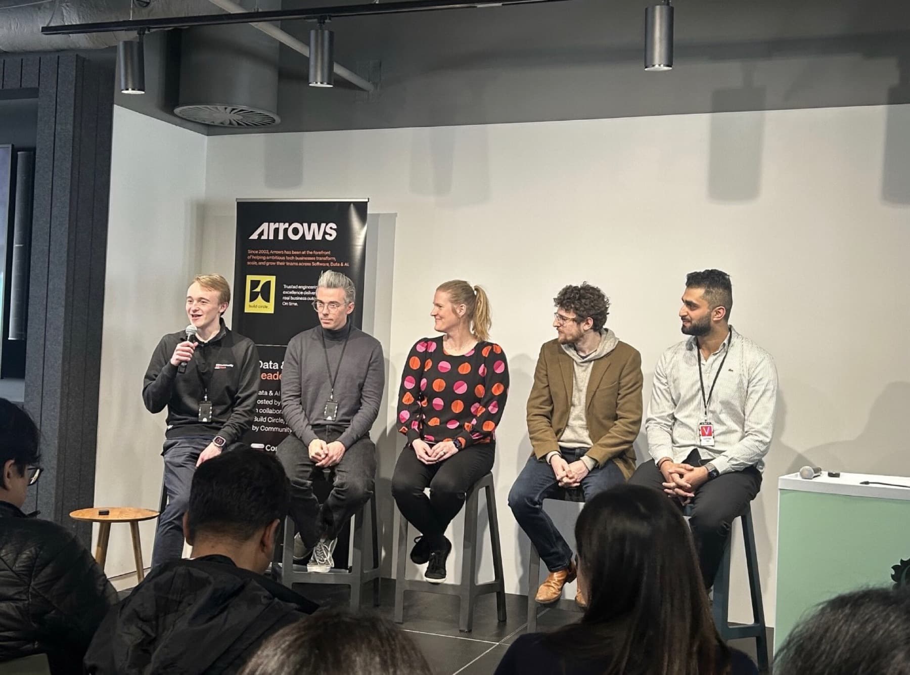 Five panellists on stools in front of an Arrows banner