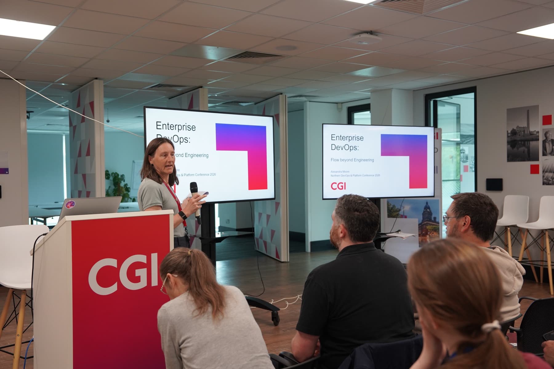 A speaker presenting on stage beside the CGI banner